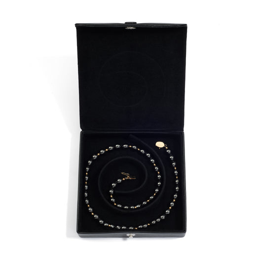 An open black medium jewelry box containing a coiled pearl necklace, neatly arranged in the spiral groove.
