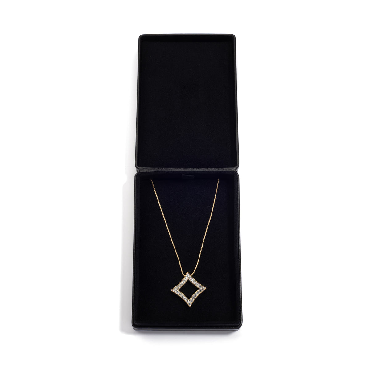 An open black jewelry box displaying a gold necklace with a diamond-shaped pendant, neatly positioned inside the box on a black cushioned lining.