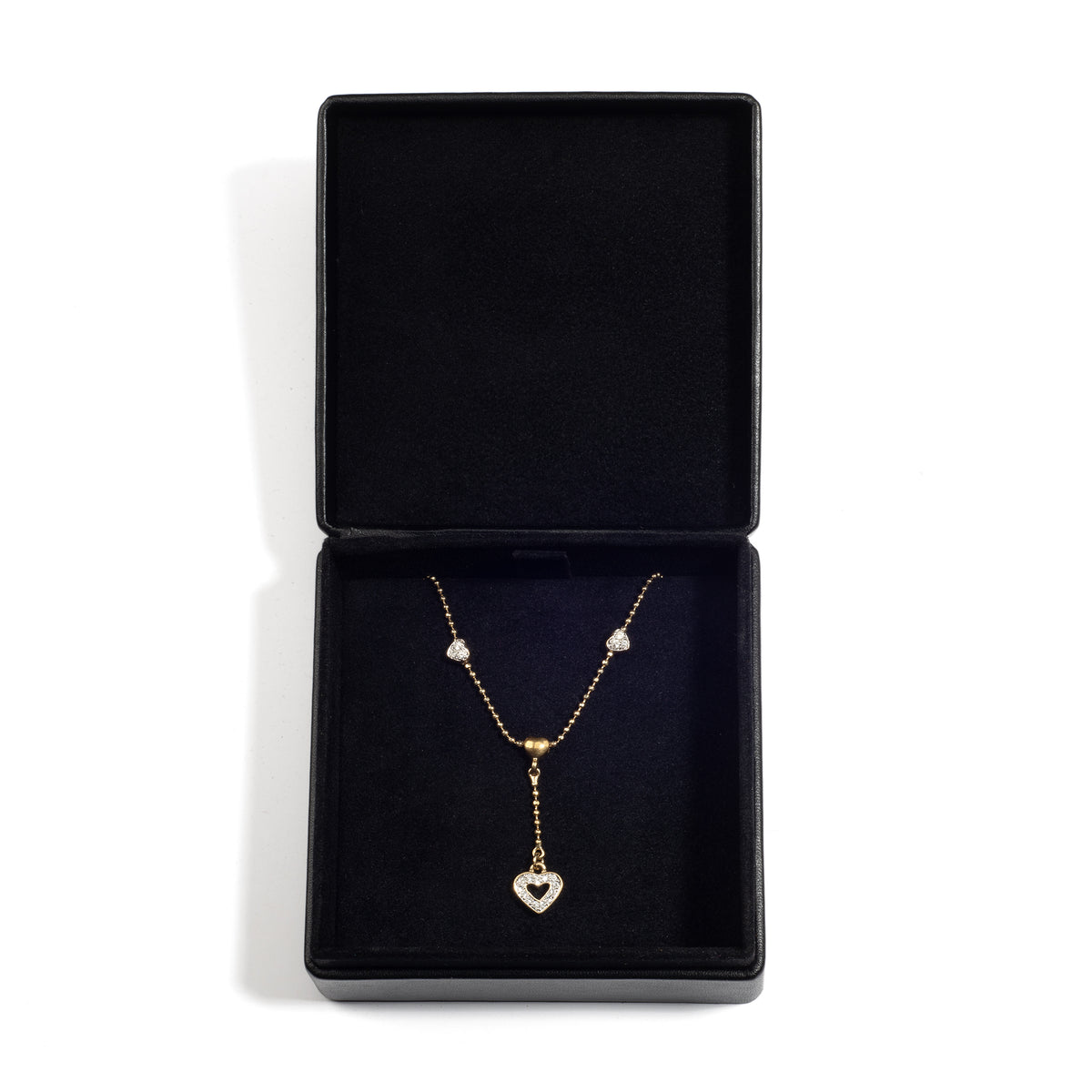 An open black jewellery box containing a gold necklace with a heart-shaped pendant and small decorative charms, resting on a black velvet lining.