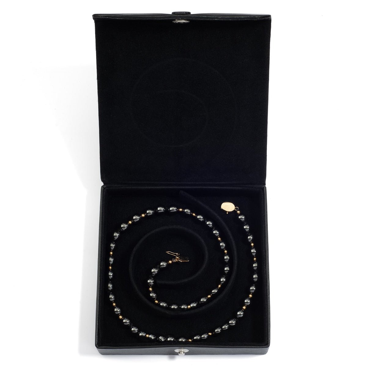 An open black medium jewelry box containing a coiled pearl necklace, neatly arranged in the spiral groove.