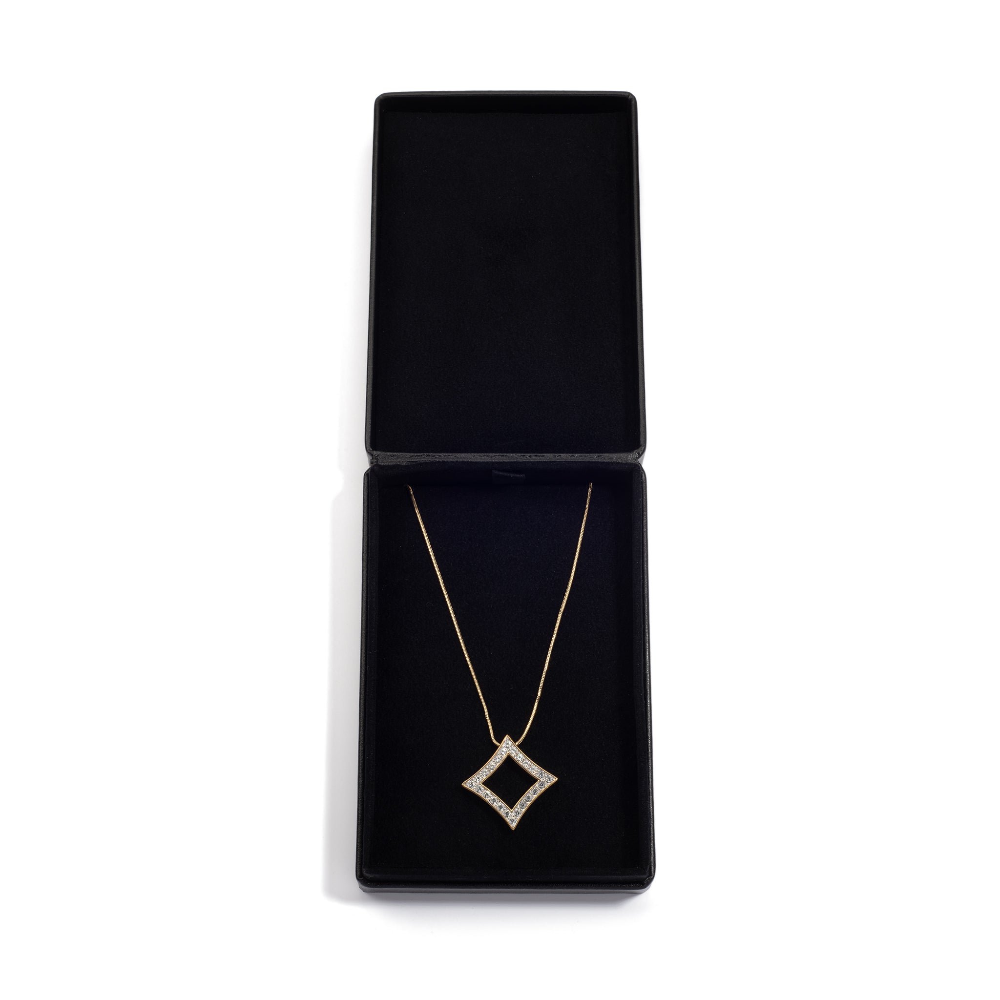 An open black jewelry box displaying a gold necklace with a diamond-shaped pendant, neatly positioned inside the box on a black cushioned lining.