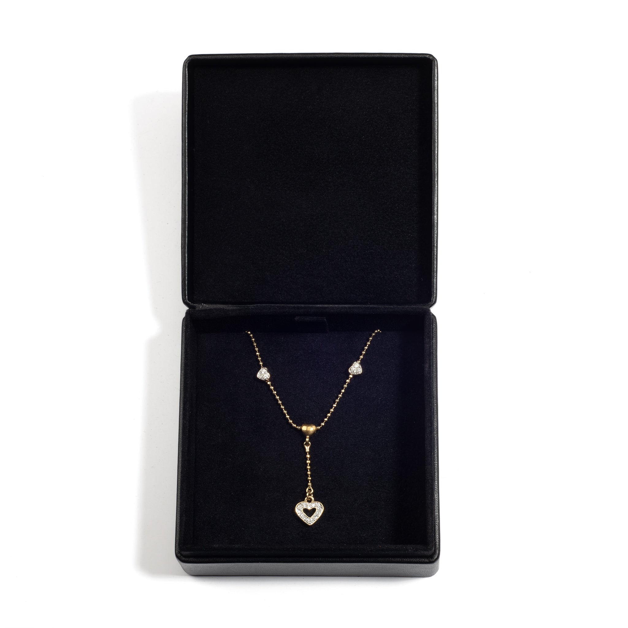 An open black jewellery box containing a gold necklace with a heart-shaped pendant and small decorative charms, resting on a black velvet lining.